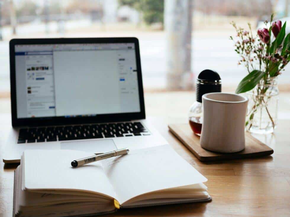 laptop computer with notepad in front, on a desk, with flowers and a mystery drink - maybe coffee, maybe tea - off to the right