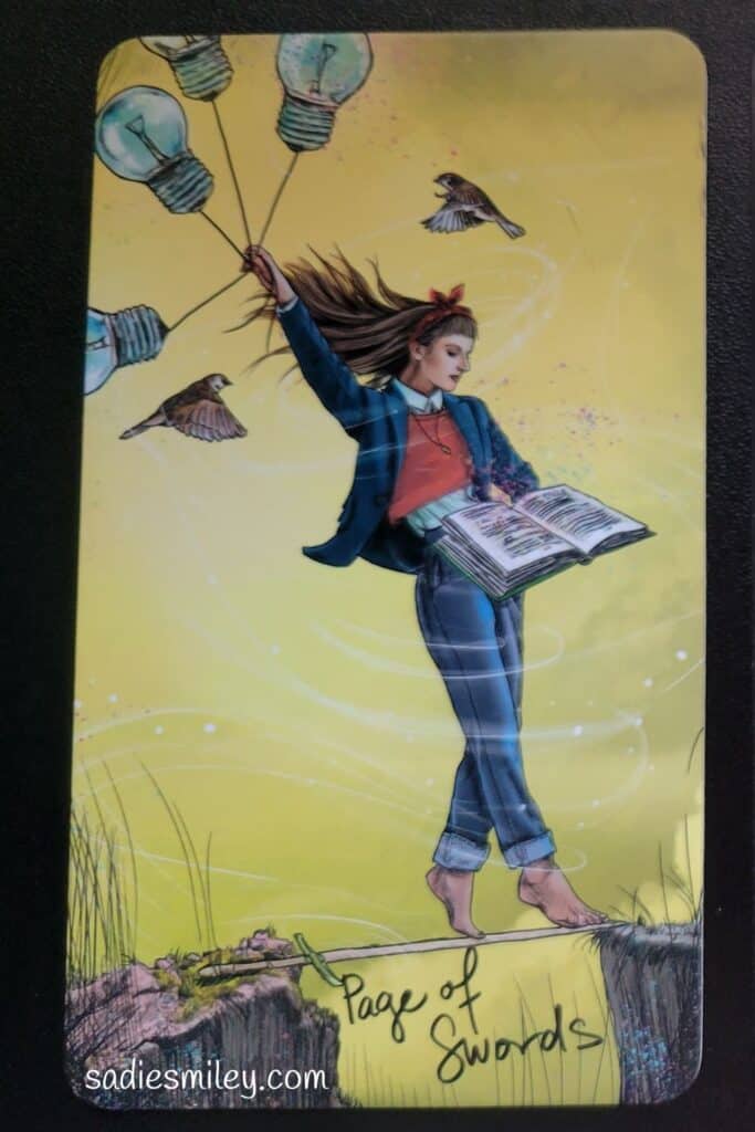 Page of Swords Tarot Card: she is holding lightbulbs (all of her many ideas), a book (a journal to write them down), and birds surround her